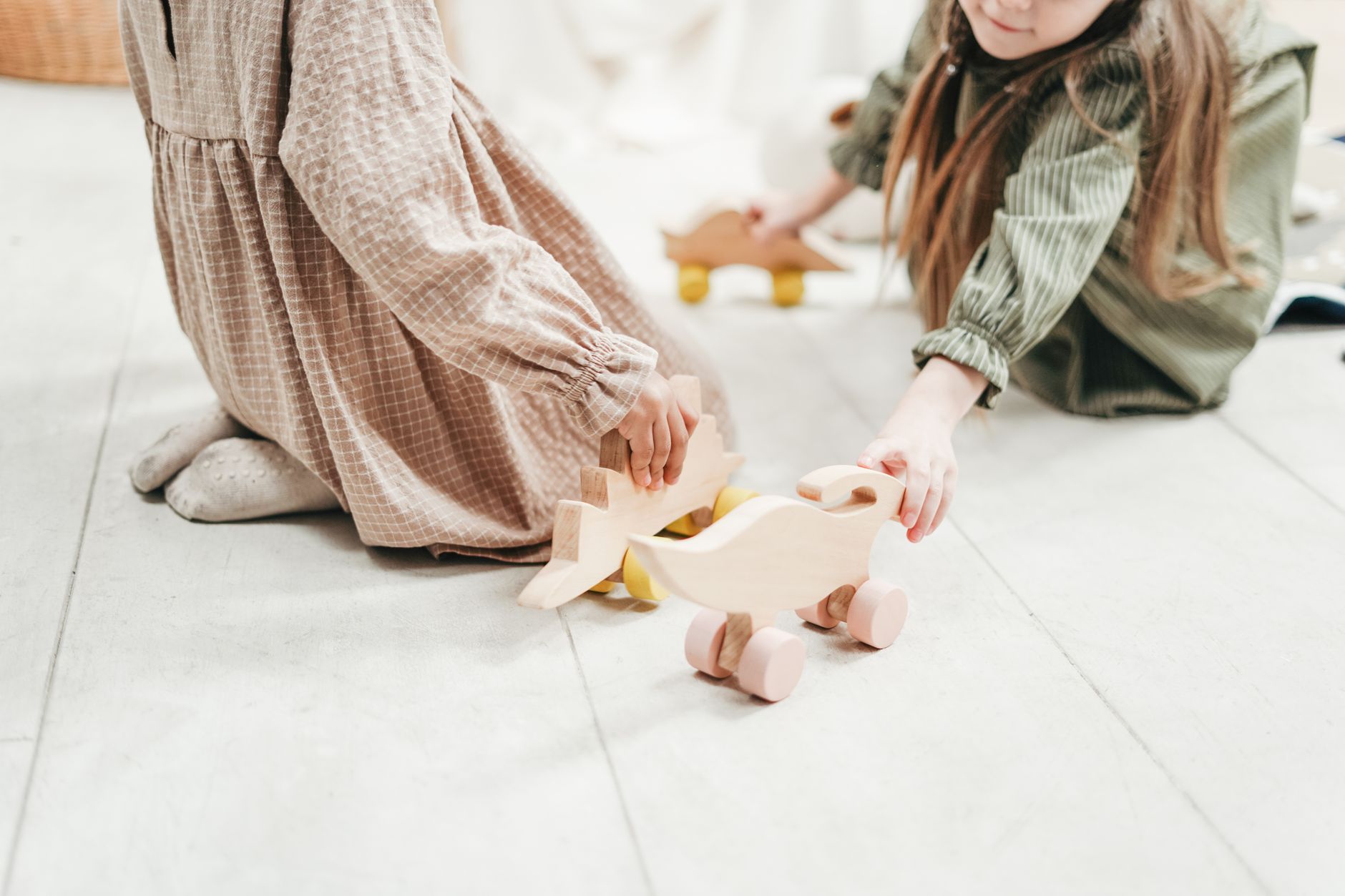 Two children kneeling on a pale floor pushing small wooden animal toys