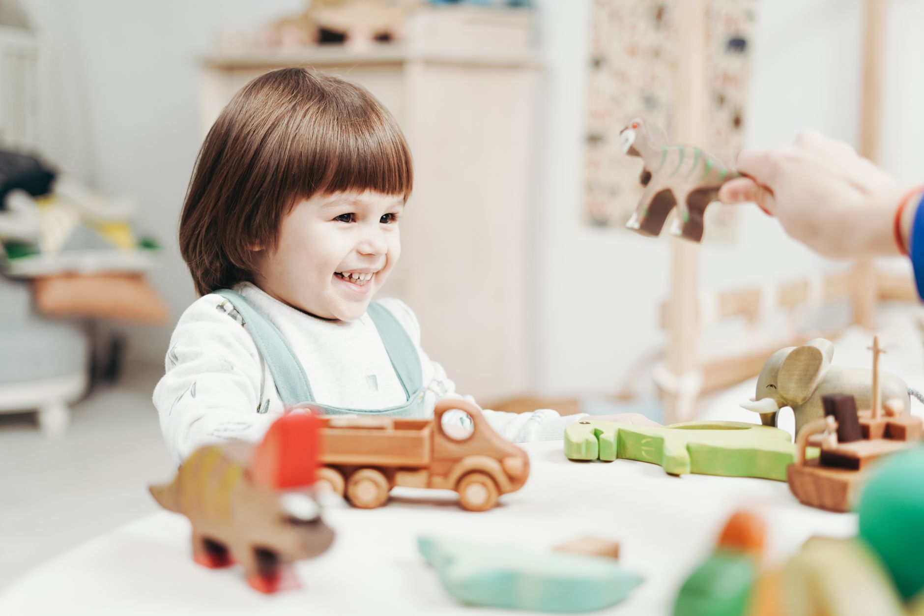 A smiling toddler playing with wooden toy vehicles and animals at a low table