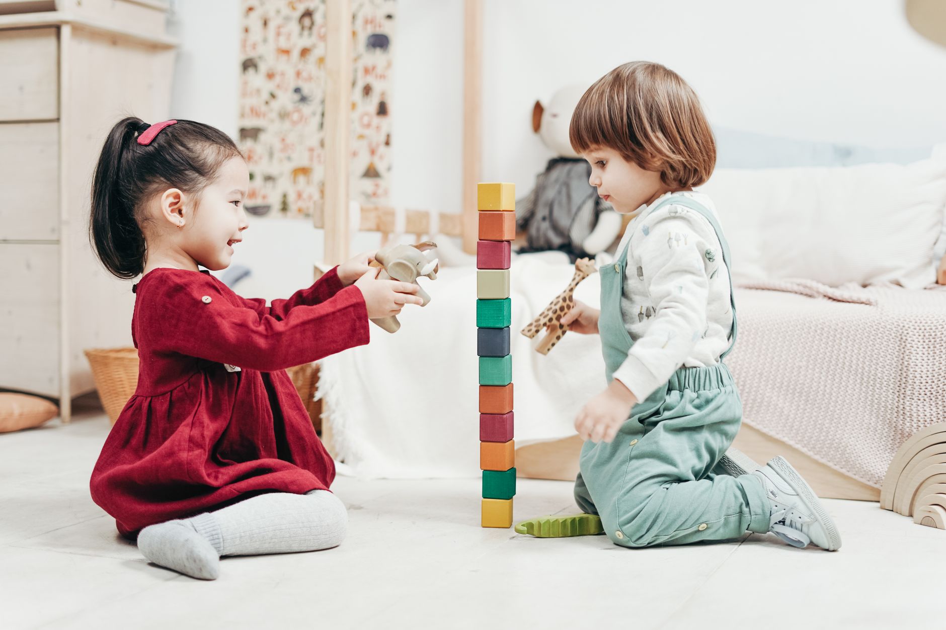 Two toddlers stacking coloured wooden blocks together on a pale floor
