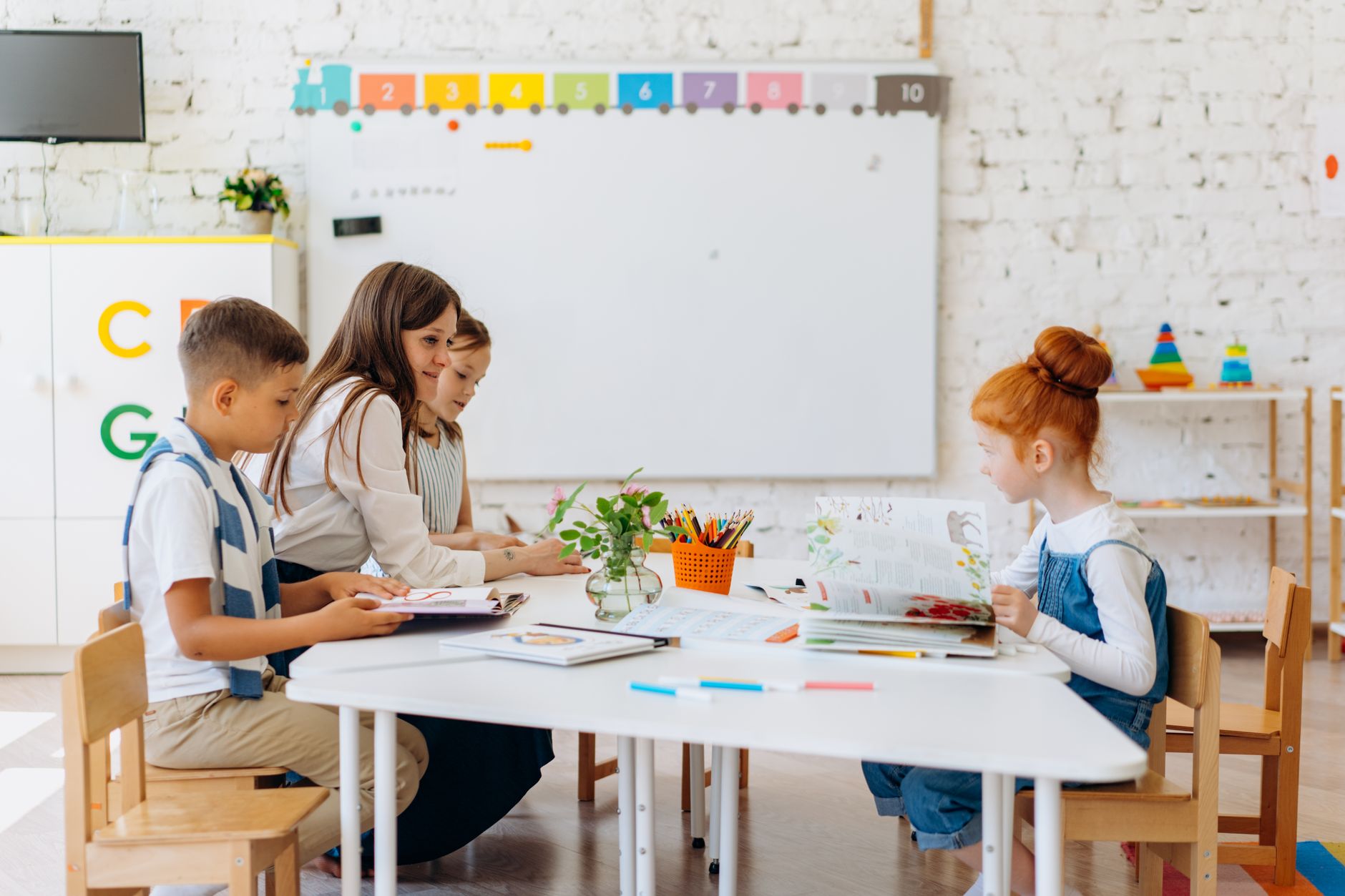 A teacher and older preschool children working together at a table in a bright classroom