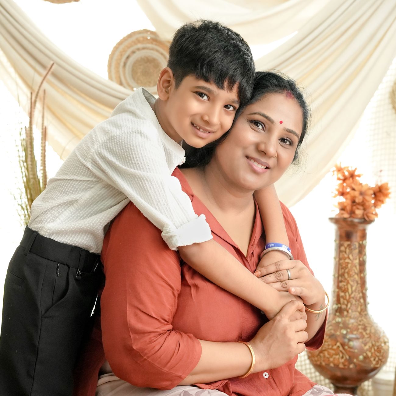 A smiling mother hugged from behind by her young son